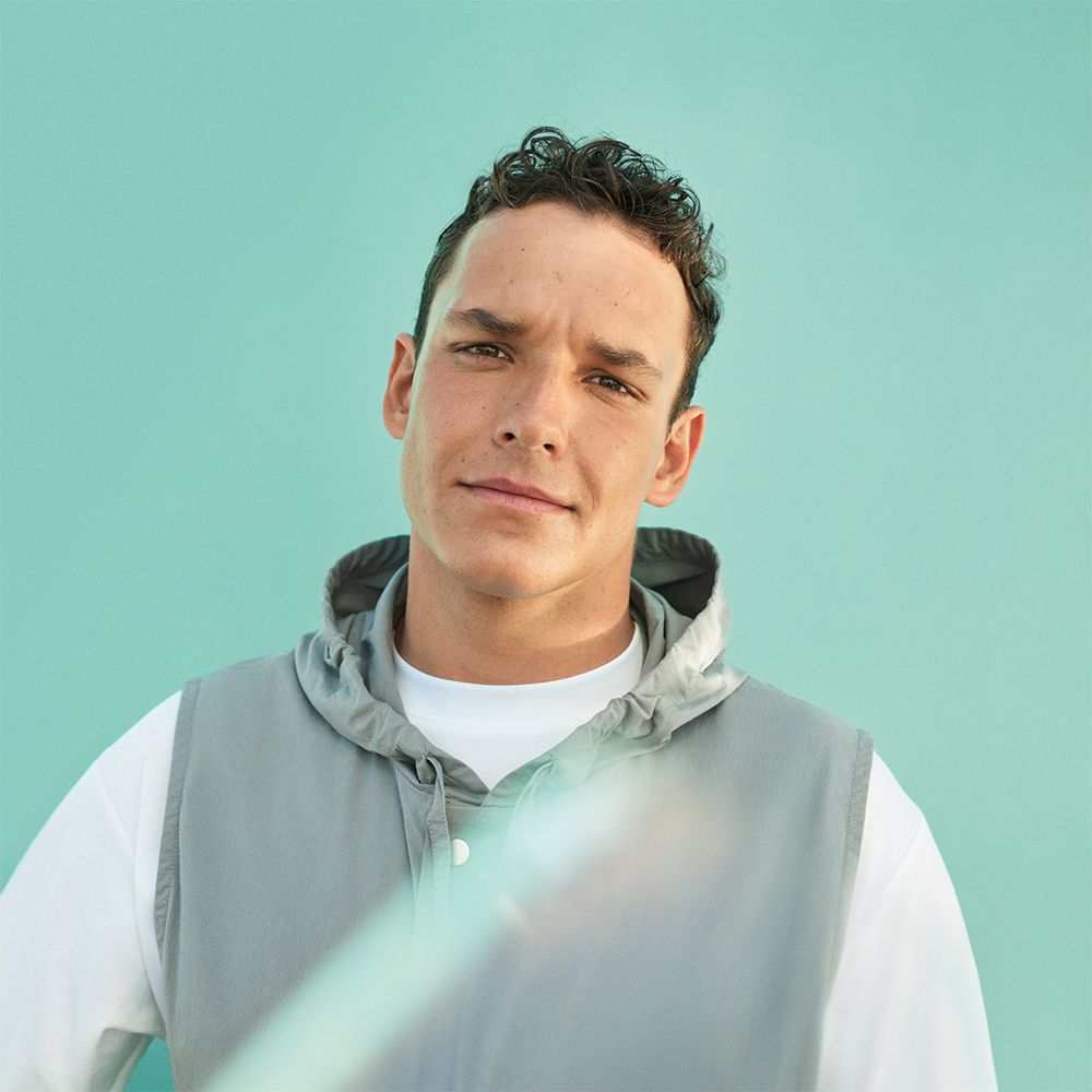 Ritratto di un uomo. Indossa una felpa grigia con cappuccio e guarda la fotocamera.