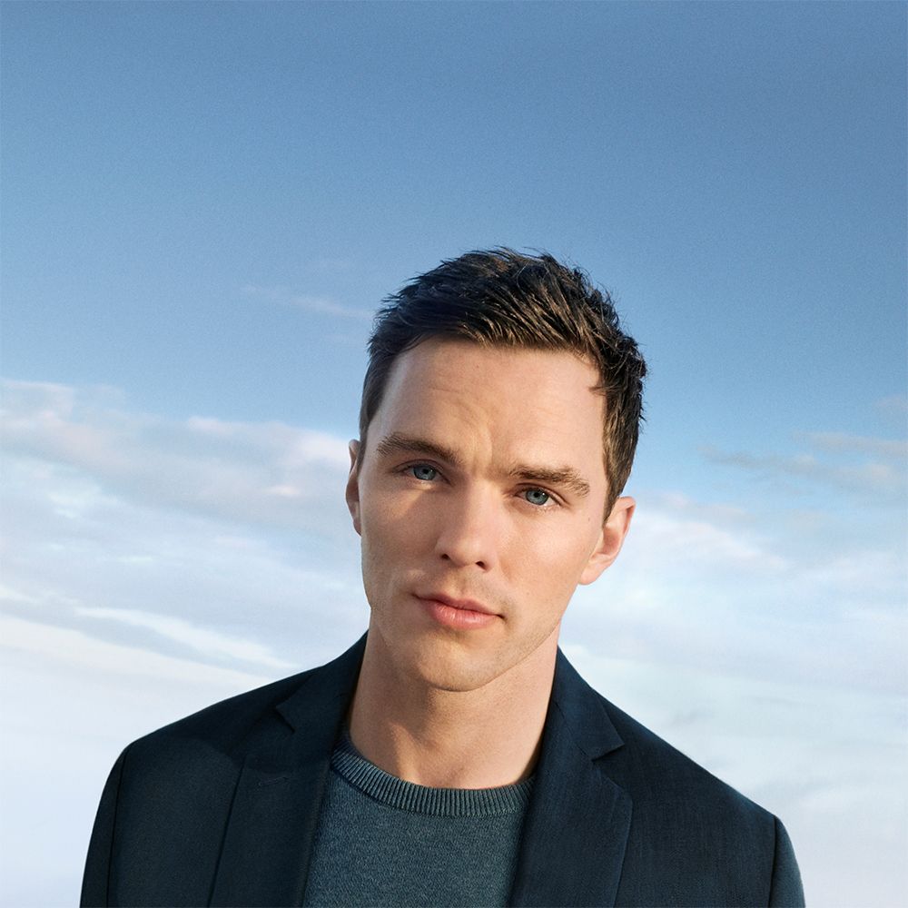 Ritratto di un uomo davanti a un cielo blu. Indossa un blazer scuro e un maglione grigio.