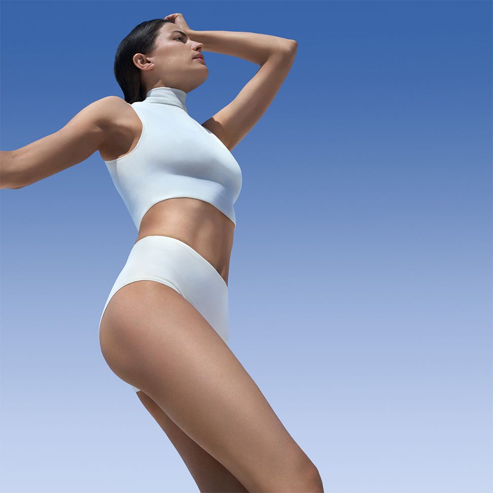 Donna in abiti bianchi su sfondo blu. Guarda in alto, mano sulla testa.