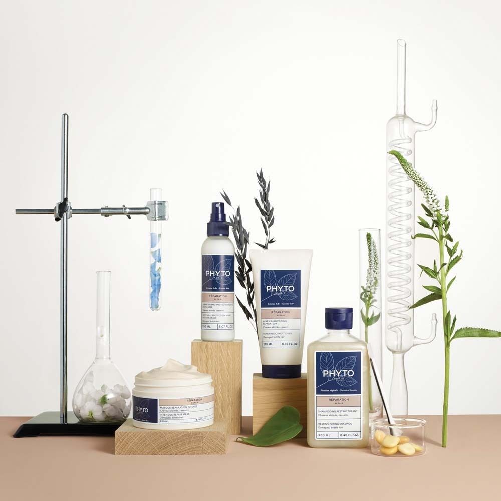 Tre prodotti per capelli Phyto: una crema, uno spray e una bottiglia di shampoo, disposti con attrezzature di laboratorio e piante.