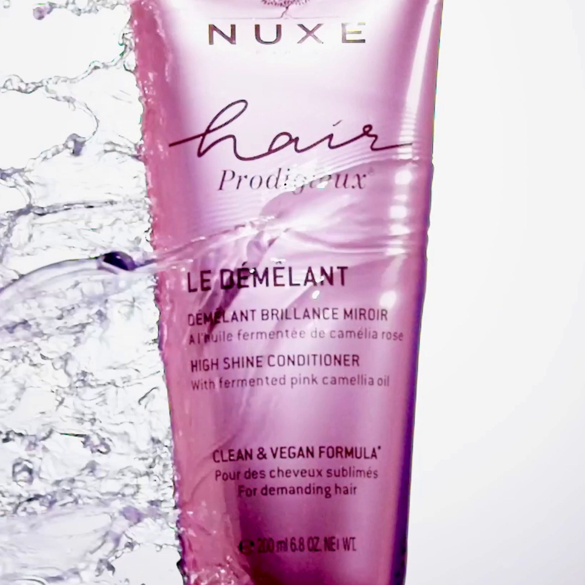 Tubo rosa NUXE Hair Prodigieux circondato dall'acqua. Testo sul tubo.