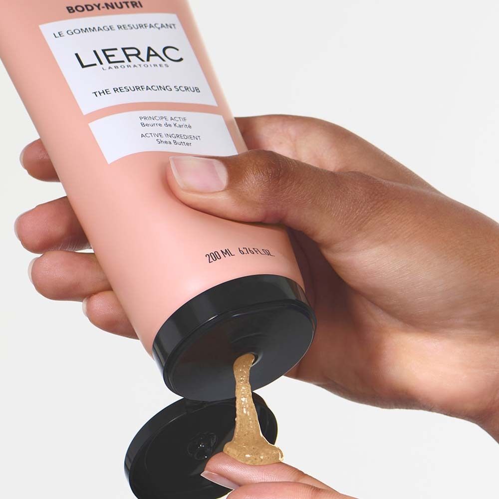 Mano che preme scrub da tubo rosa. Scritta: BODY-NUTRI, LIERAC, THE RESURFACING SCRUB.