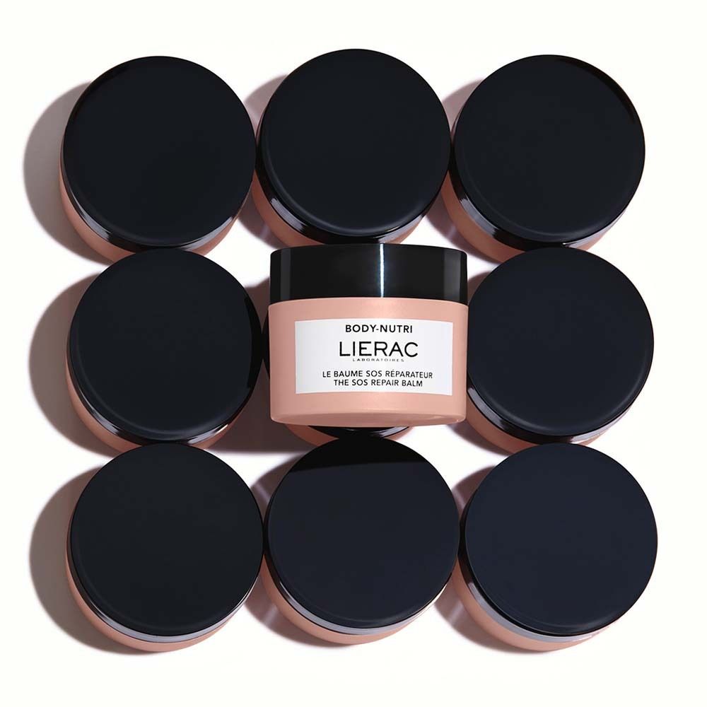 Otto vasetti con coperchi neri circondano un vasetto con etichetta bianca. Scritta: LIERAC, LE BAUME SOS RÉPARATEUR, THE SOS REPAIR BALM.