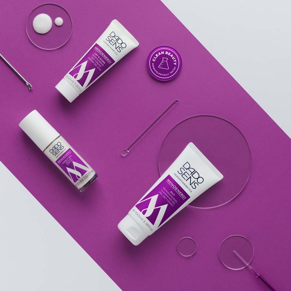 Vari prodotti DADO SENS su sfondo viola. Prodotti: crema occhi, gel detergente, siero, crema. Accessori: spatole, contenitori rotondi.