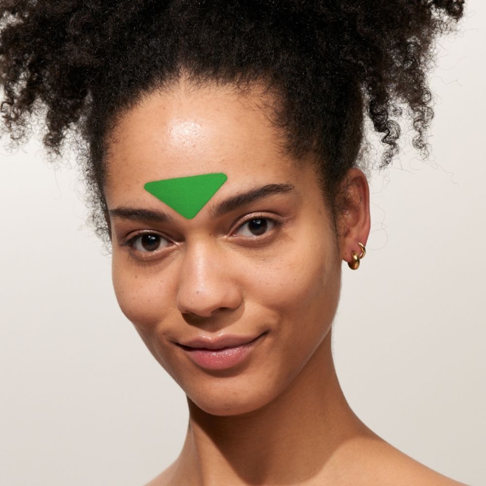 Donna con un patch viso verde a forma di triangolo con Aloe Vera sulla fronte.