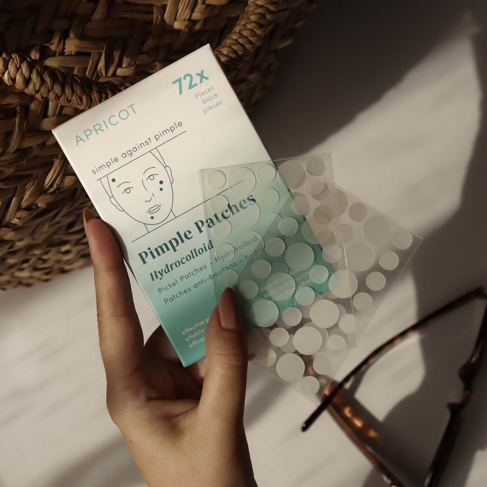 Mano che tiene una confezione di cerotti per brufoli. Marchio APRICOT. 72 pezzi. Cerotti idrocolloidi.
