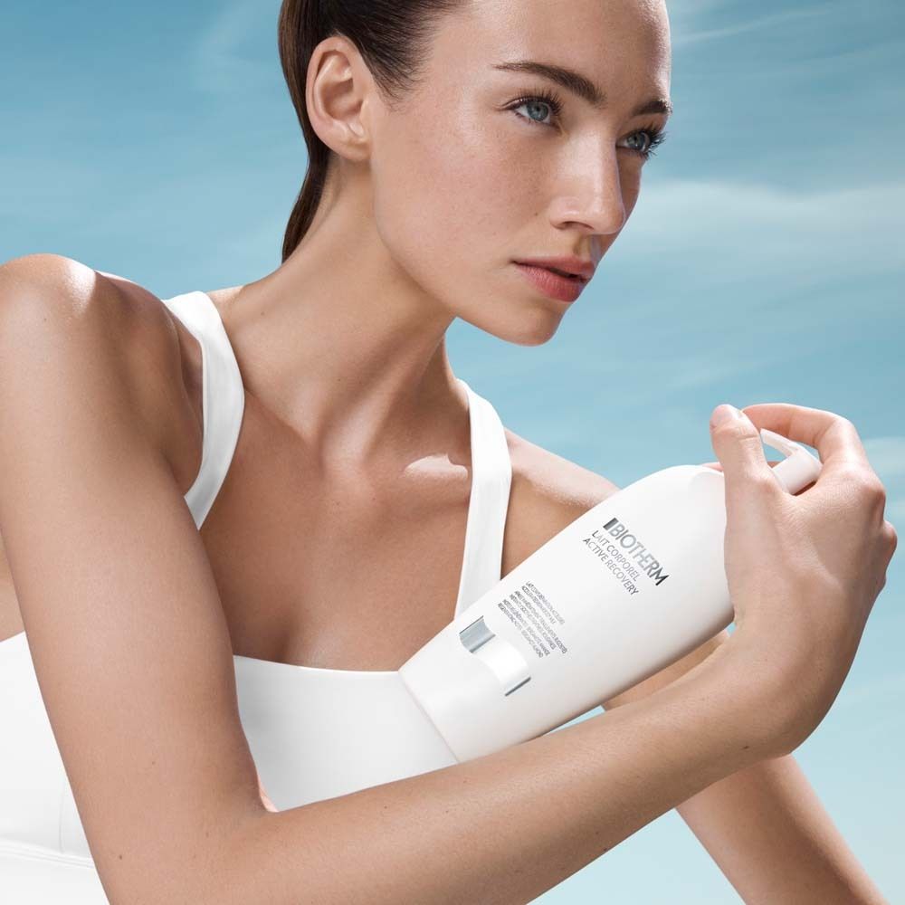 Donna che tiene in mano un flacone bianco con dosatore. Scritta: Biotherm Lait Corporel Active Recovery.