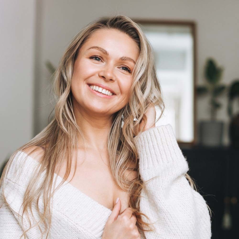 Giovane donna bionda sorridente. Indossa un maglione bianco.
