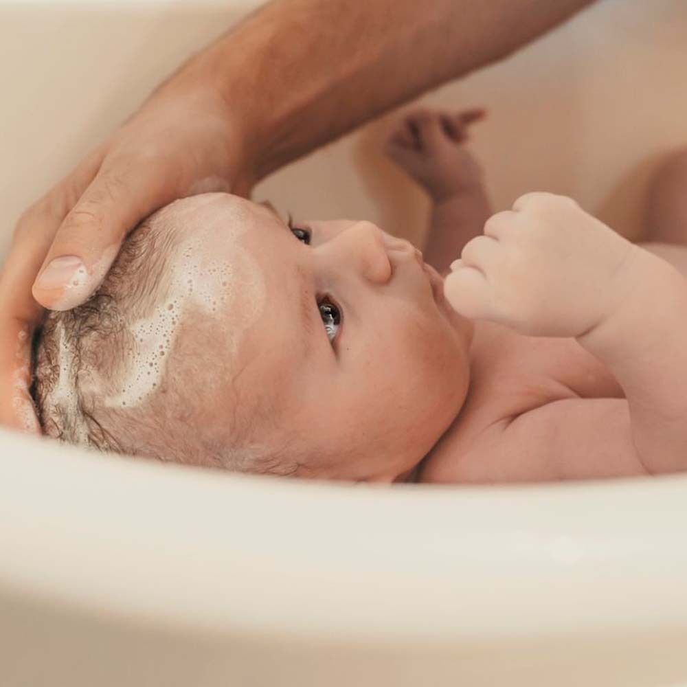 Bambino nella vasca da bagno. Una mano lava i capelli del bambino con la schiuma.