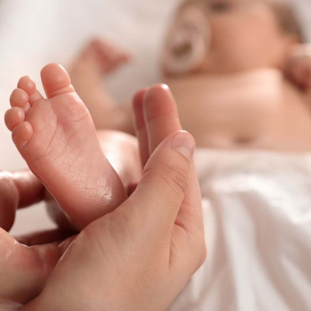 Primo piano di un piede di bambino in una mano. Il piede è leggermente oliato.