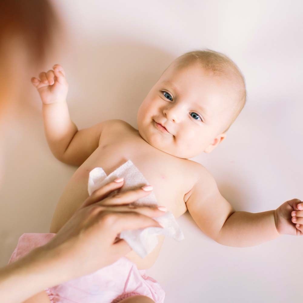 Bambino supino, una mano pulisce il busto con un panno bianco. Pannolino rosa.