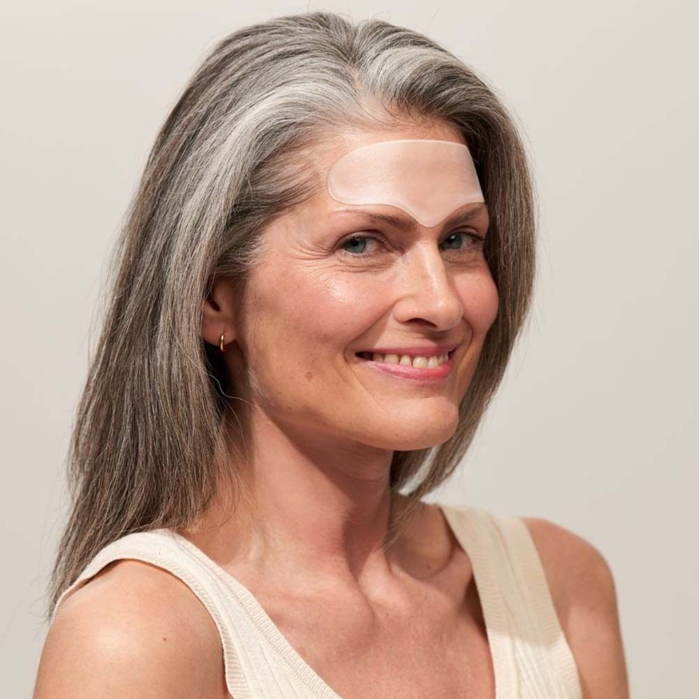 Donna con Forehead Pad sulla fronte. Pad trasparente. Capelli grigi. Top beige.