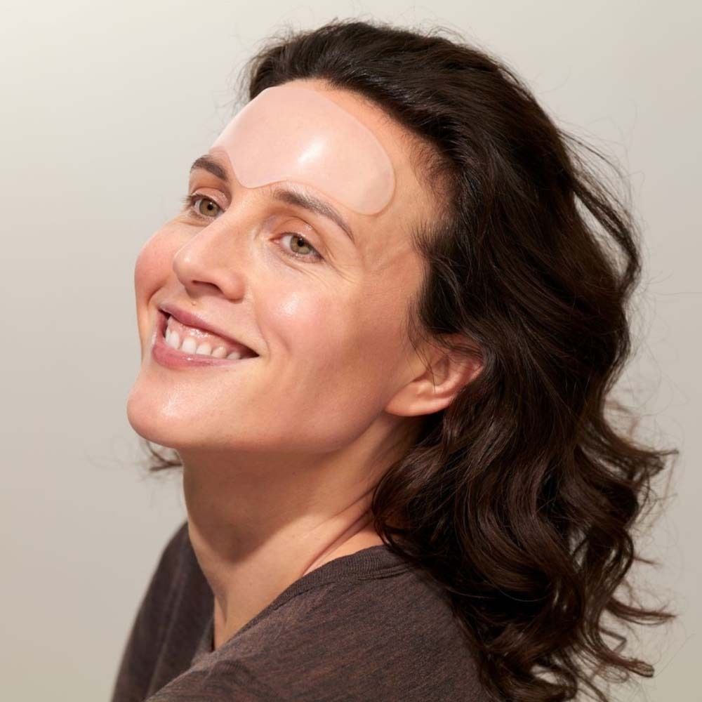 Donna con pad per la fronte sulla fronte. Pad trasparente. La donna sorride. Capelli castani, top marrone.