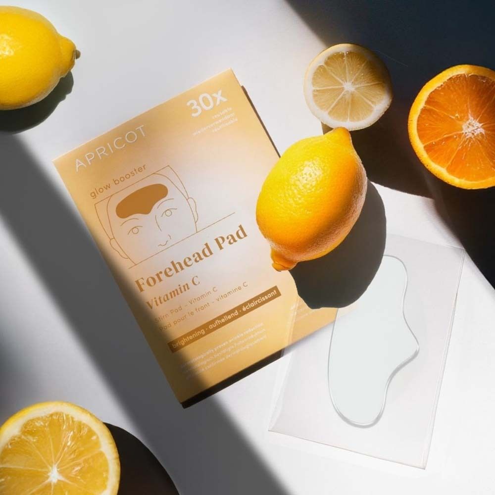 Pad per la fronte con vitamina C e confezione. Limoni e arancia accanto. Testo: APRICOT, Forehead Pad, 30x.