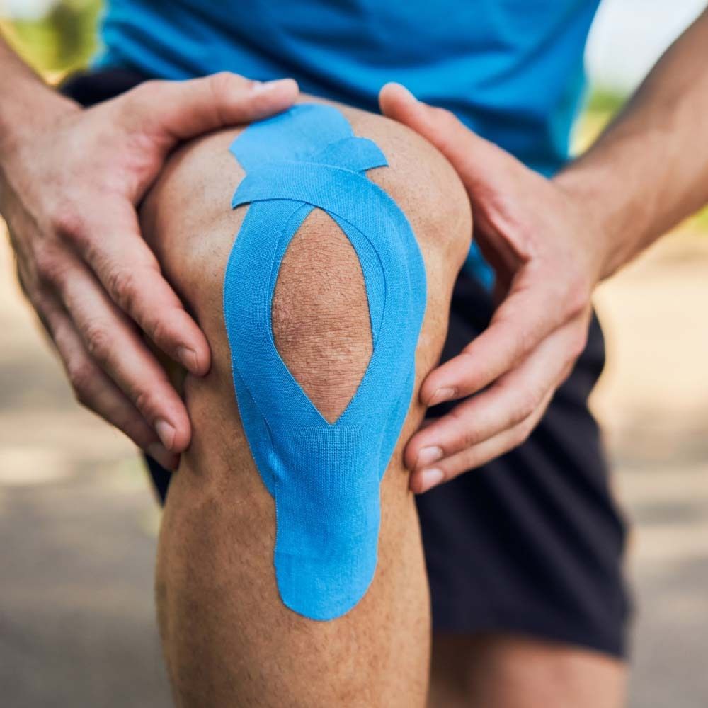 Ginocchio con nastro kinesiologico blu applicato. Mani che tengono il ginocchio.