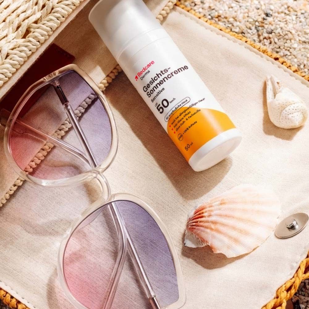 Flacone di crema solare, occhiali da sole e conchiglia su una borsa da spiaggia. Sfondo spiaggia.