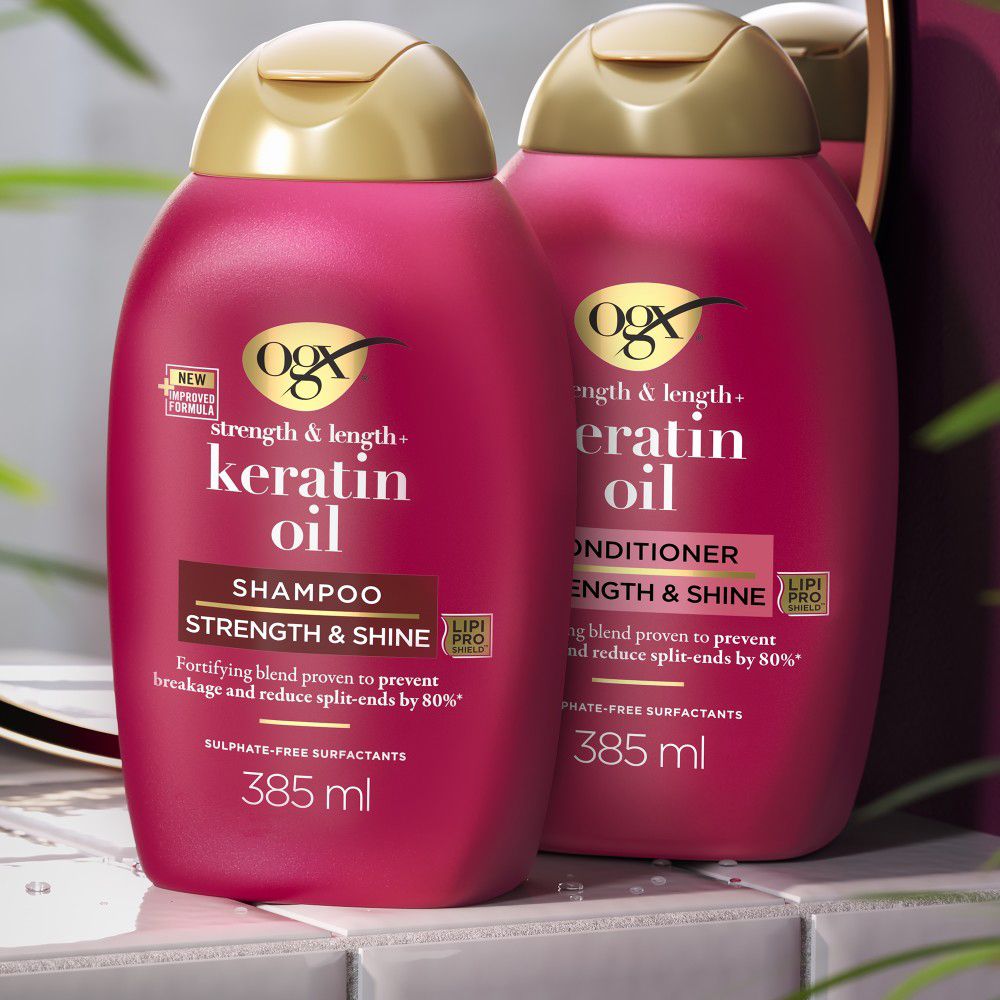 Due flaconi di shampoo rossi con tappi dorati. Testo: OGX, Keratin Oil, Shampoo, 385 ml.