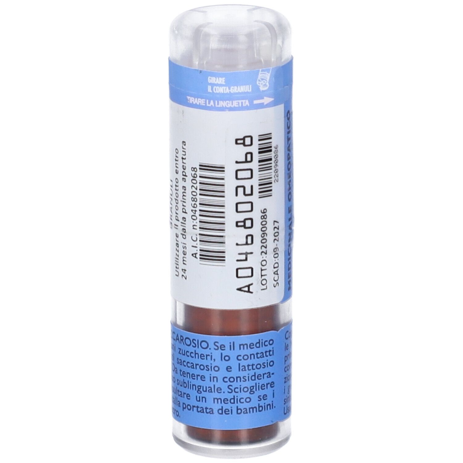 Flacone cilindrico multidose. Etichetta blu e bianca con testo. Tappo trasparente. Granuli marroni visibili.