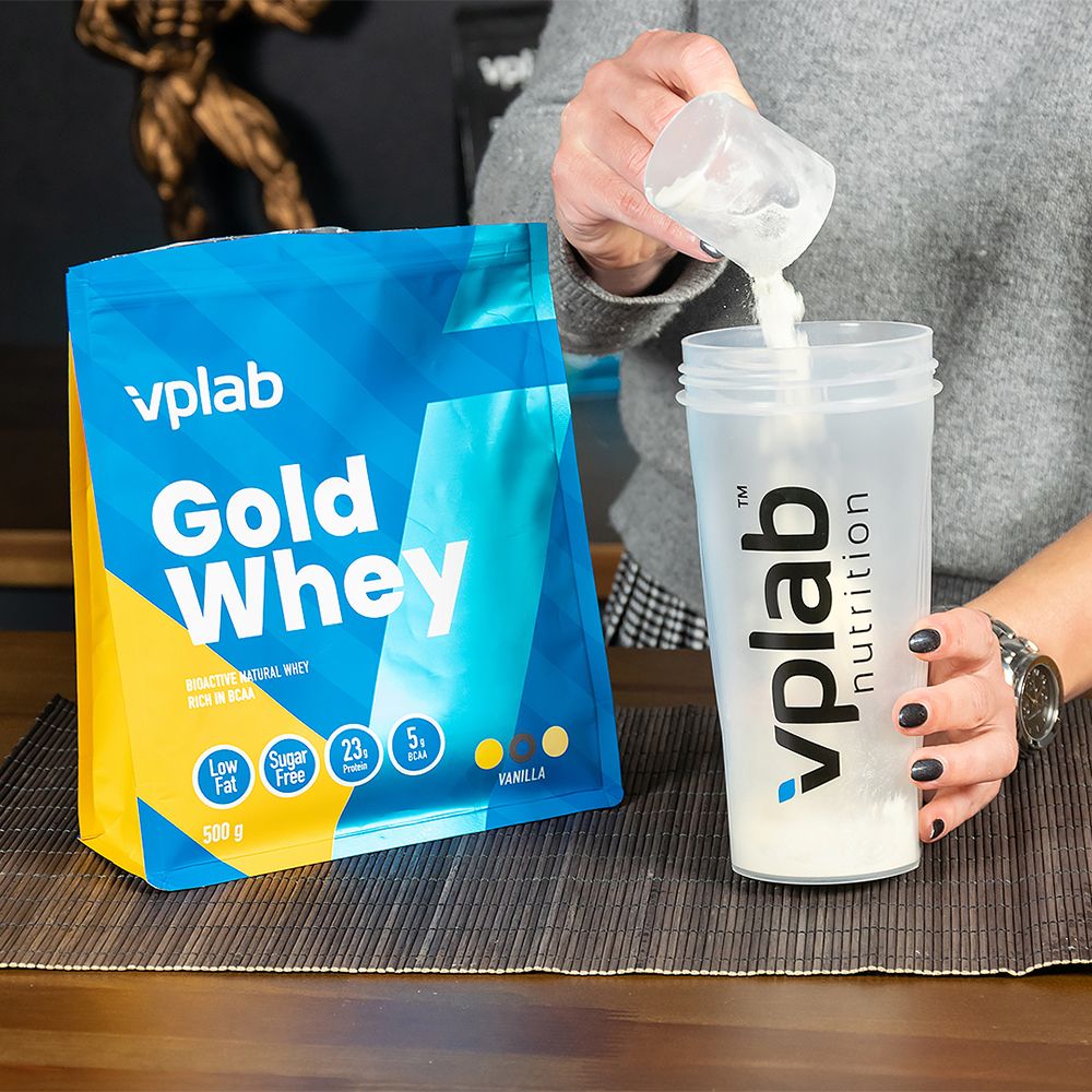 Persona versa polvere da un misurino in uno shaker. Accanto, confezione 'vplab Gold Whey'.