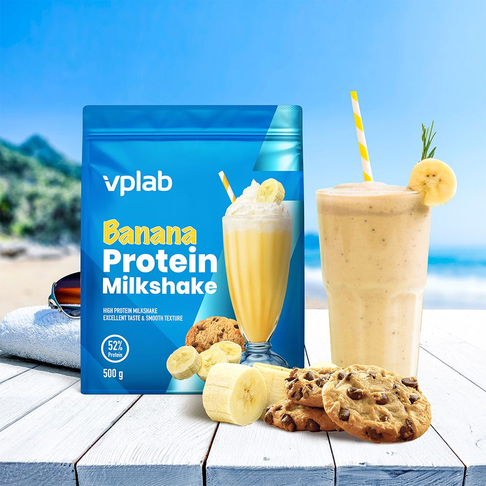 Confezione blu "Vplab" con "Banana Protein Milkshake". Accanto: milkshake, banana, biscotti, sfondo spiaggia.