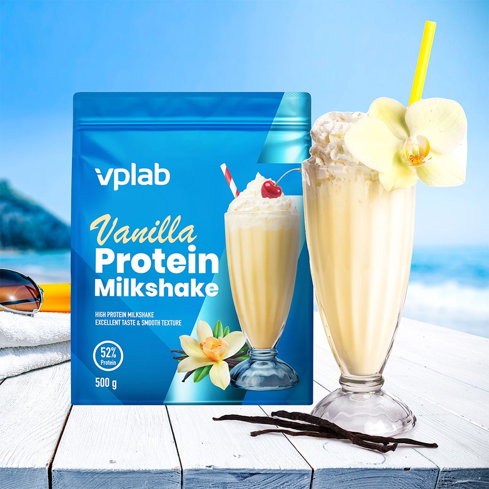 Bicchiere di milkshake con panna e ciliegia. Accanto, una busta « Vplab Vanilla Protein Milkshake ». Su un tavolo sulla spiaggia.