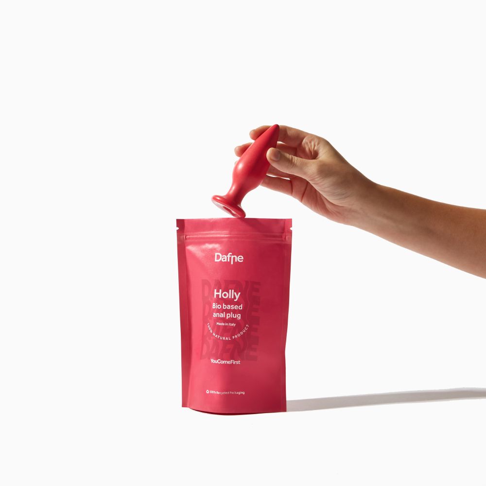 Mano che posiziona un plug anale rosso in una confezione rosa. Testo sulla confezione.