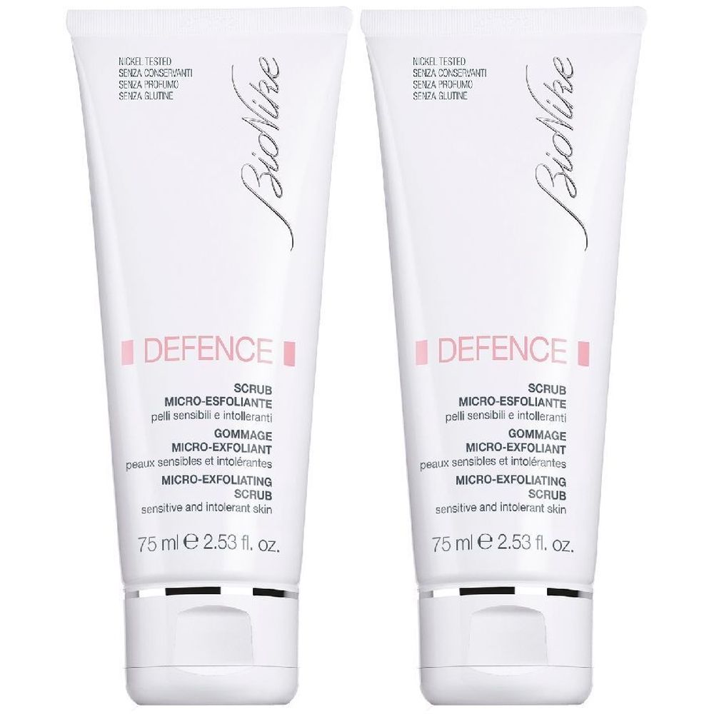Due tubi bianchi con testo rosa. Scritto: Defence Scrub Micro-Esfoliante. In basso: 75 ml 2.53 fl. oz.