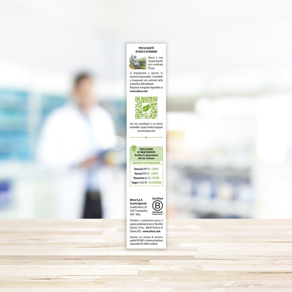 Confezione prodotto stretta con testo e codice QR. Sfondo: farmacia sfocata.
