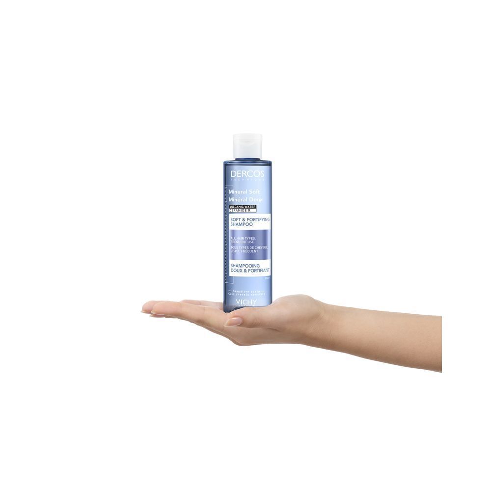 Una mano tiene una bottiglia di shampoo. Scritta: Dercos, Mineral Soft, Shampoo.
