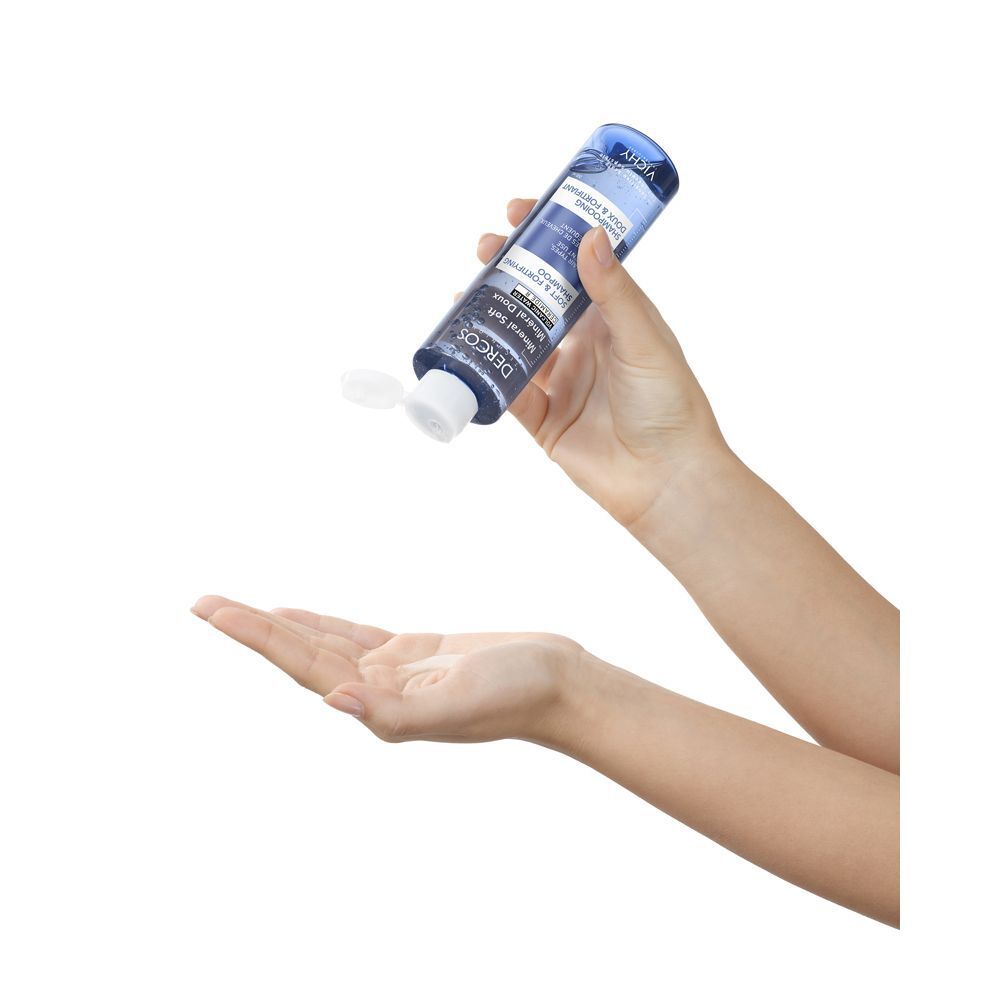 Mani che tengono una bottiglia di shampoo. Scritta: Dercos, Mineral Soft, Shampoo. Bottiglia aperta.