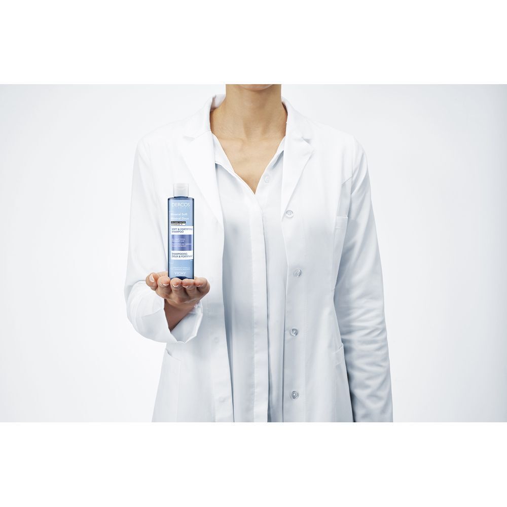 Persona in camice bianco che tiene una bottiglia di shampoo. Scritta: Dercos, Mineral Soft, Shampoo.