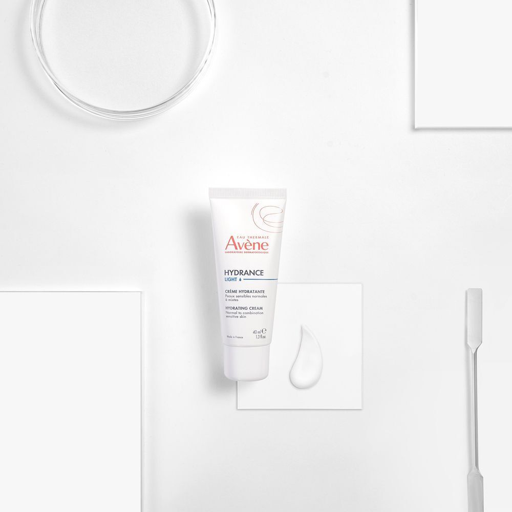 Tubo di crema Avène Hydrance Light su sfondo bianco. Con goccia di crema e spatola.