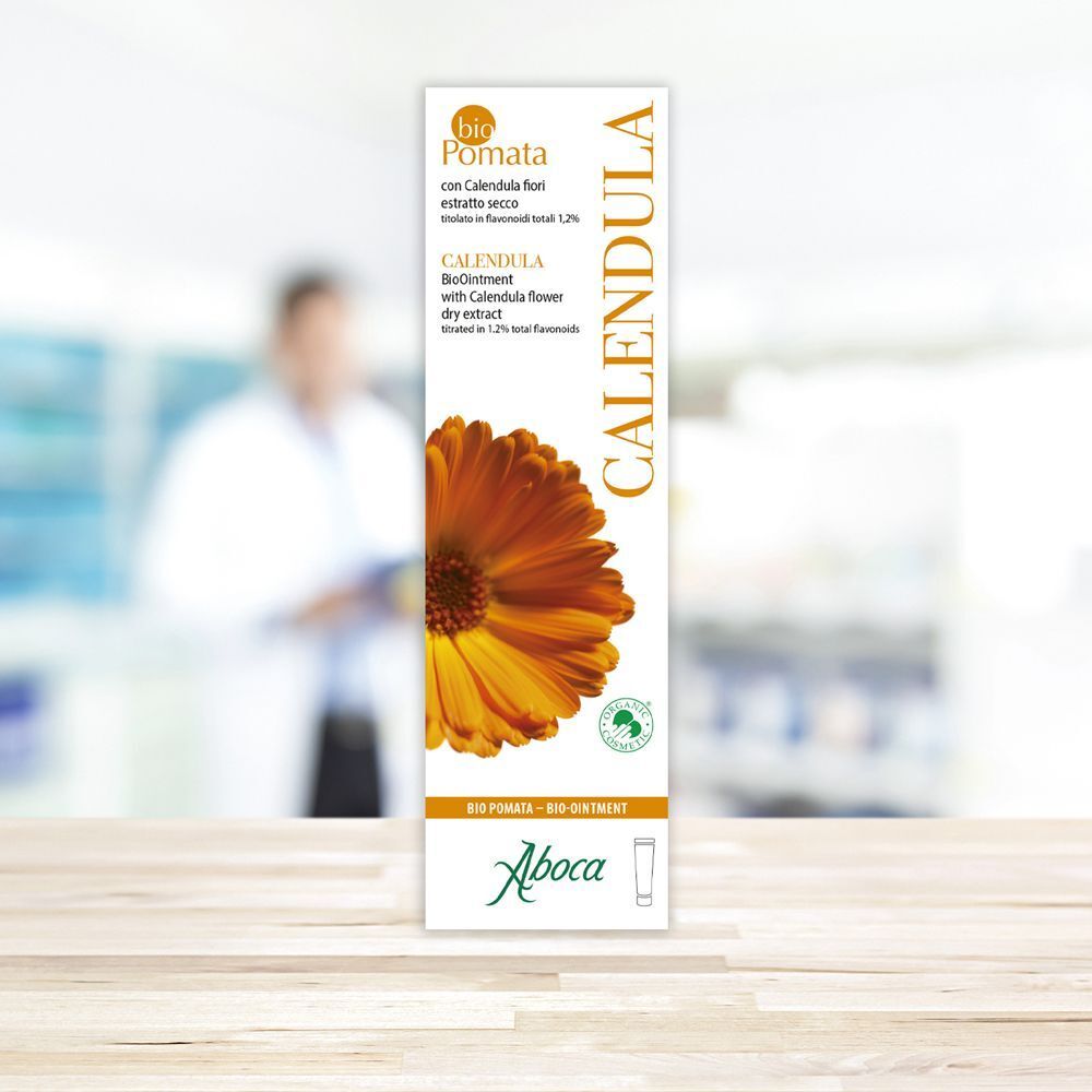 Confezione rettangolare con scritta CALENDULA, fiore di calendula e logo Aboca. Sfondo: persona sfocata in laboratorio.