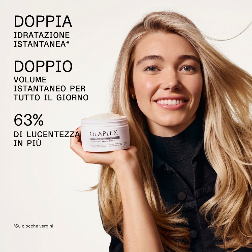 Una donna sorridente con capelli biondi tiene in mano un vasetto di Olaplex Weightless Nourishing Mask.