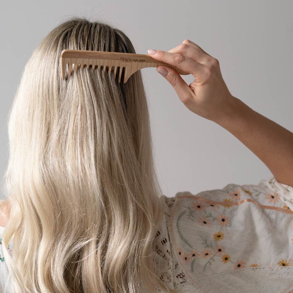 Mano che pettina capelli biondi con un pettine in legno a denti larghi. Il pettine ha un manico curvo.