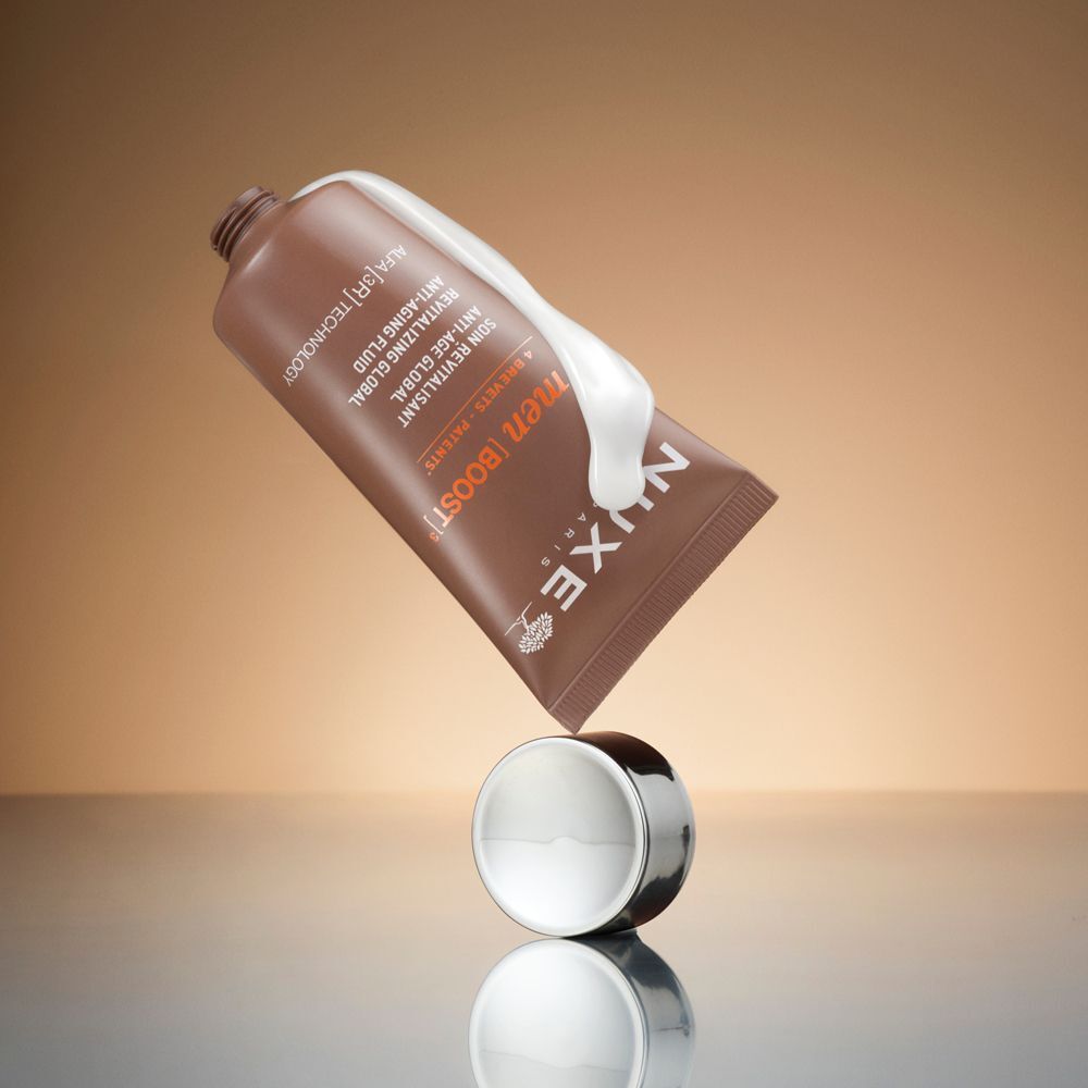 Un tubo marrone di Fluido Anti-Età Nuxe Men con tappo argentato, accanto a una crema bianca.