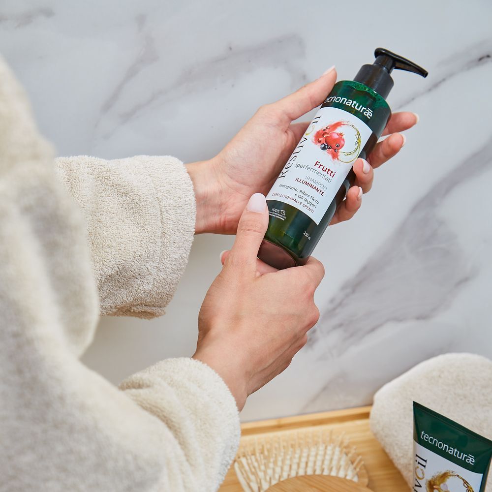 Mani che tengono un flacone di Restivoil Tecnonaturae Shampoo Illuminante in un ambiente bagno.