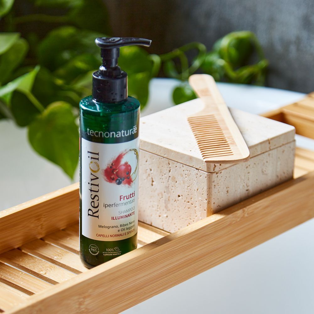Restivoil Tecnonaturae Shampoo Illuminante su un ripiano in bambù con pettine e scatola di pietra.