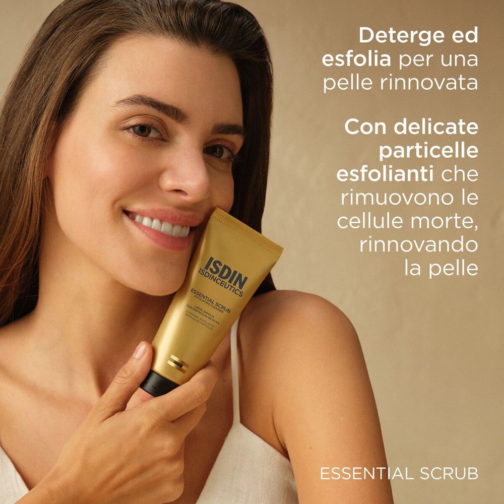 Donna sorridente tiene un tubo dorato ISDIN Isdinceutics Essential Scrub vicino alla guancia. Testo in italiano.