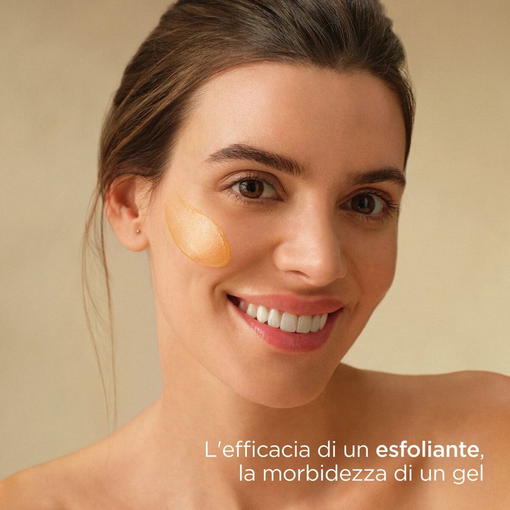 Donna sorridente con ISDIN Isdinceutics Essential Scrub sulla guancia. Testo in italiano.