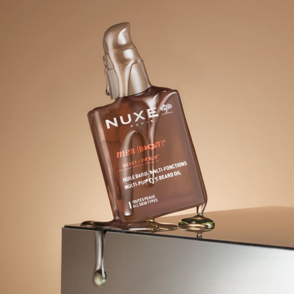 Un flacone di olio da barba Nuxe Men inclinato, con olio che cola su una superficie liscia.