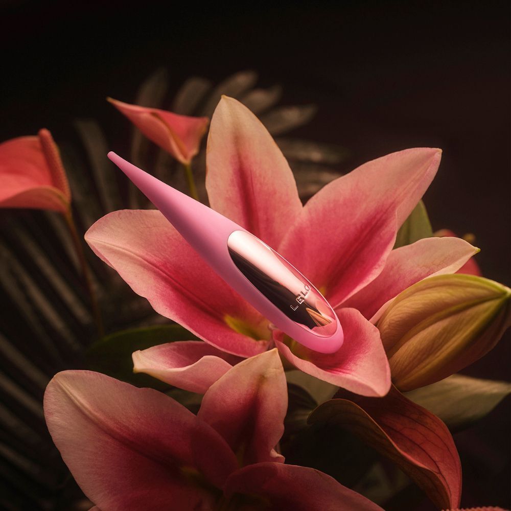 Vibratore viola su un giglio rosa con sfondo scuro.