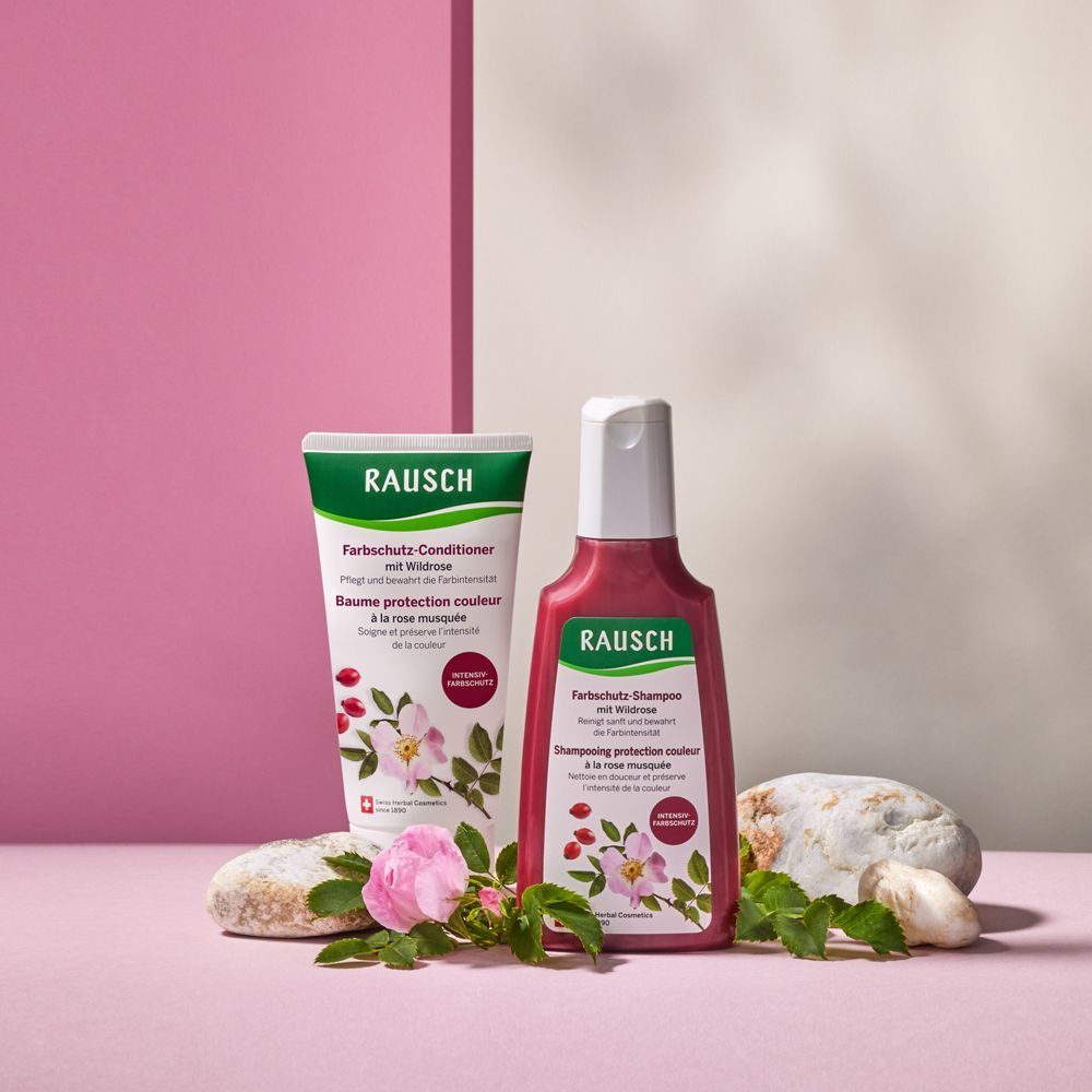 Flacone di balsamo e shampoo RAUSCH alla rosa selvatica, disposti con pietre e un fiore.