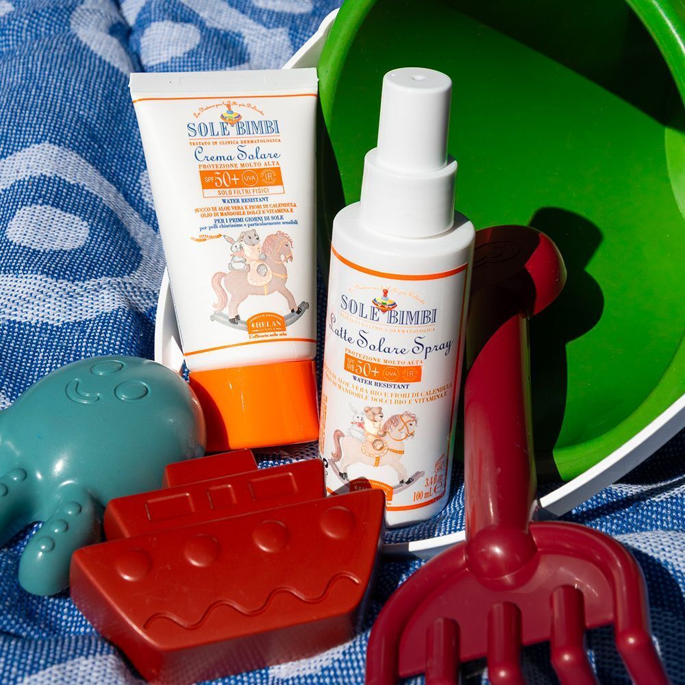 Latte solare spray SPF50+ e tubo crema solare con giochi sulla spiaggia.