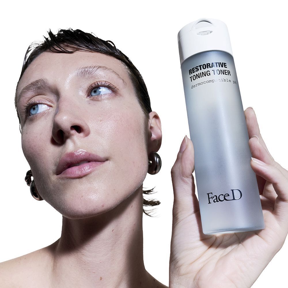 Una donna tiene in mano un flacone di Face D Restorative Toning Toner.