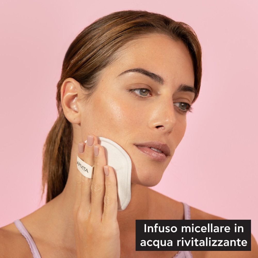 Una donna si pulisce il viso con un dischetto struccante Apivita.