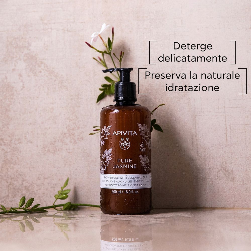 Flacone marrone con dispenser a pompa di bagnoschiuma APIVITA Pure Jasmine vicino a fiori di gelsomino.