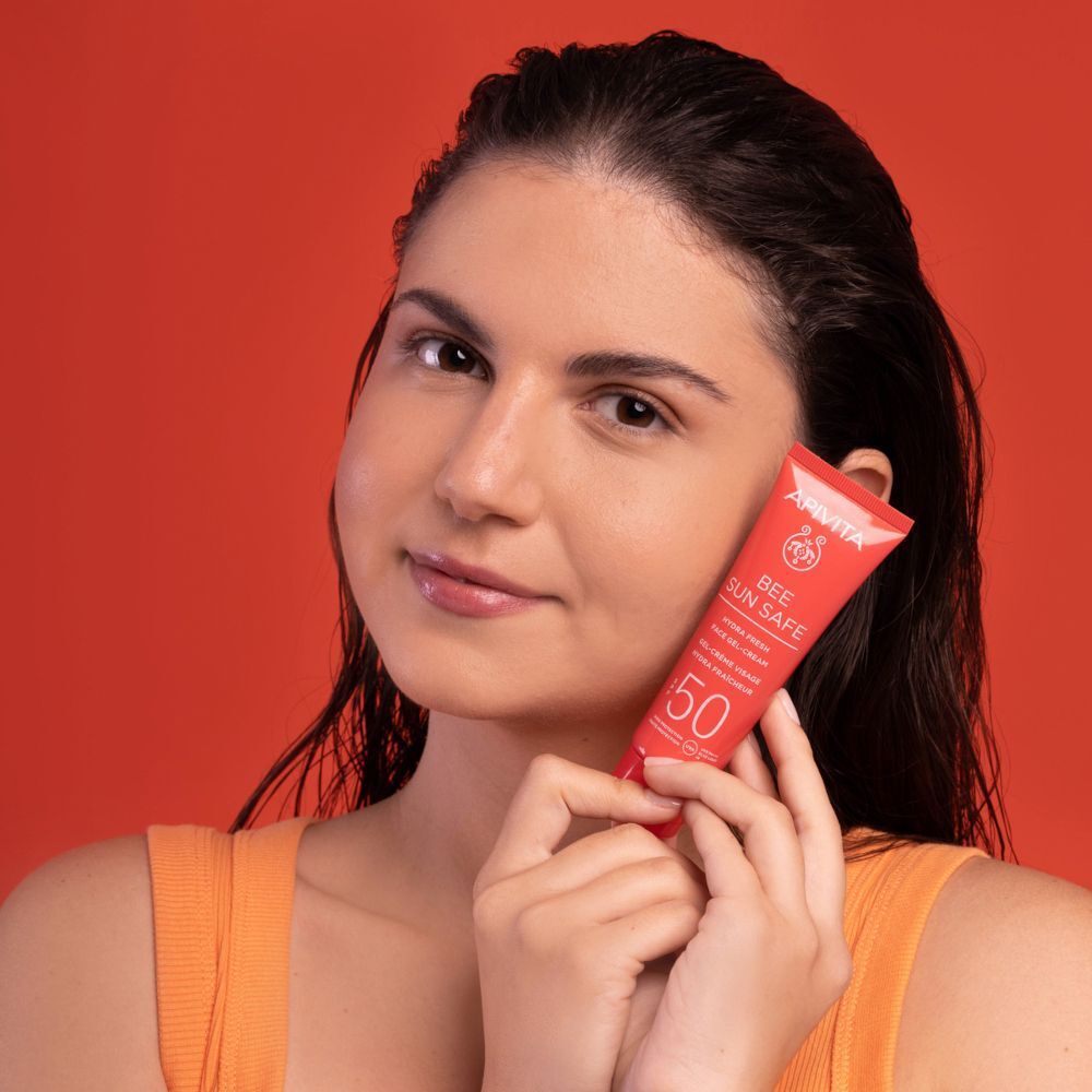 Donna tiene un tubetto rosso di crema solare SPF 50 "BEE SUN SAFE" davanti al viso.