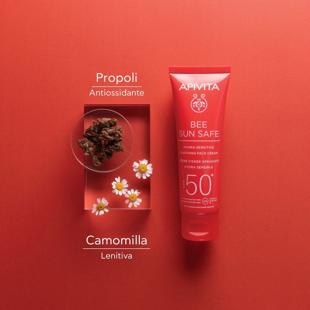 Tubetto rosso di crema solare viso APIVITA SPF 50+, vicino a fiori di camomilla e propoli.