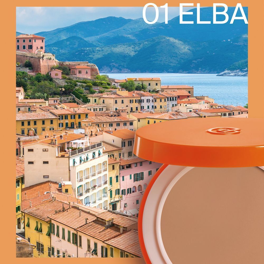Una cipria compatta aperta, contenuto marrone chiaro, davanti a un paesaggio di Elba, Italia.